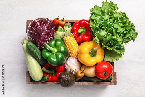Crate with different fresh vegetables on light background, top view