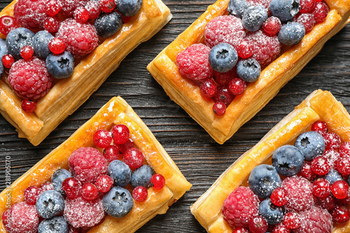 Fresh delicious puff pastry with sweet berries on dark wooden table, flat lay