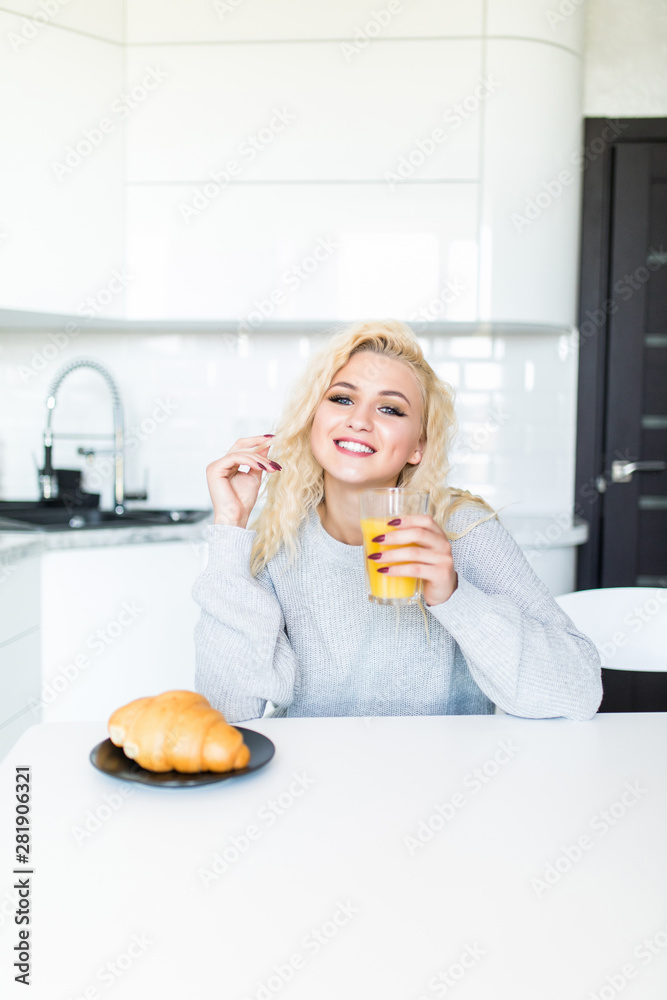 Young pretty woman with juice and croissant at kitchen table in morning