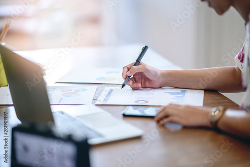 Cropped image of young businesswoman holding pen and working with chart or paperwork at office desk.