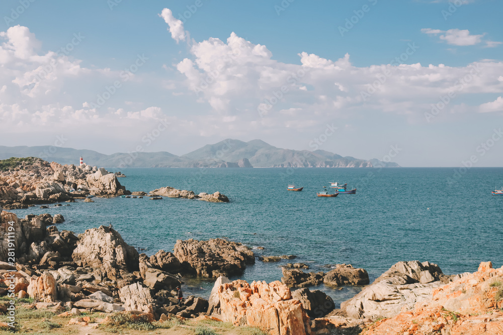 Rocky beach with calm blue sea and boats in Phu Yen, Vietnam.