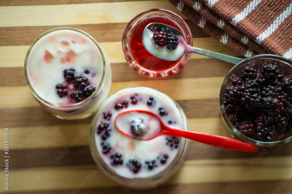 Yogurt in transparent jars with fresh blackberry and strawberry voyen with a spoon, on wooden background Yogurt in transparent jars with fresh blackberry and strawberry voyen with a spoon, on wooden background