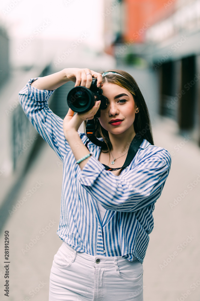 Portrait of a young woman holding camera in hand taking pictures on street walk