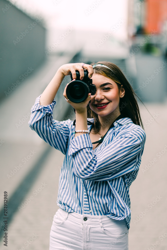 Portrait of a young woman holding camera in hand taking pictures on street walk