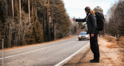 A young man is hitchhiking around the country. The man is trying to catch a passing car for traveling. The man with the backpack went hitchhiking to the south. © alexkich