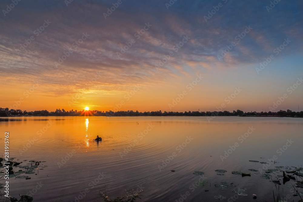 Lake view morning of a fisherman floating in water with yellow sun light and cloudy sky background, sunrise at Krajub reservoir, Ban Pong District, Ratchaburi, Thailand.