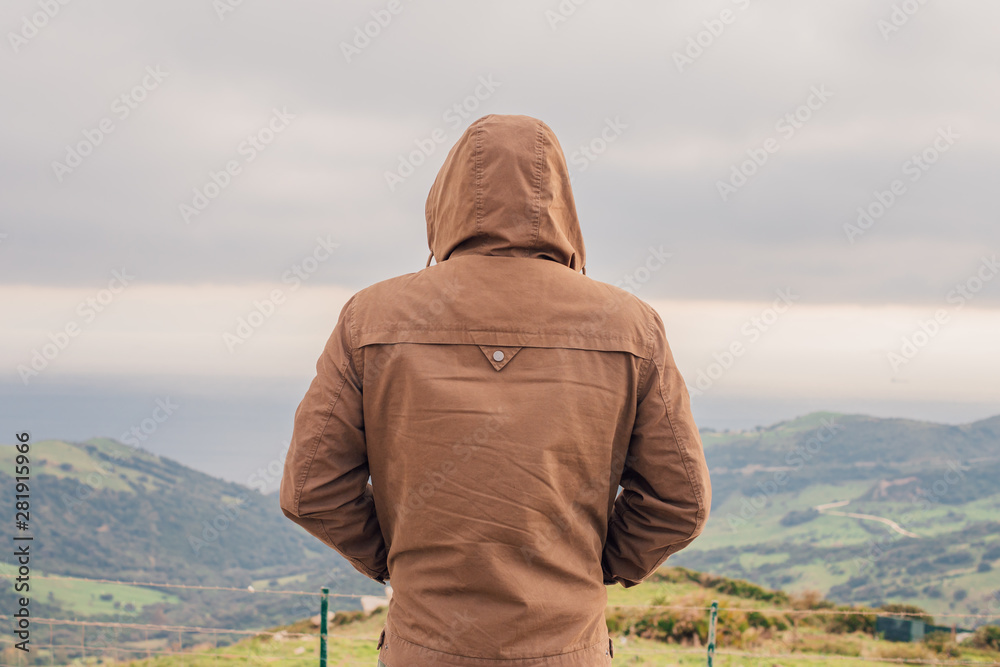 Rear view of hipster man in hood standing and watching sea and hill landscape panorama in Gibraltar