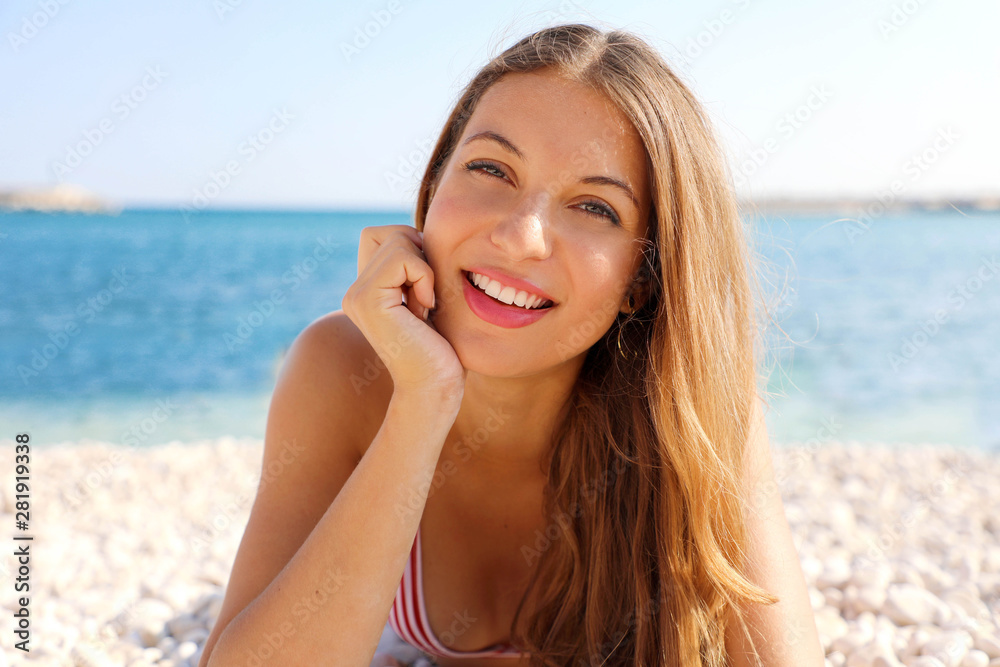 Summer holidays concept. Beauty young smiling woman enjoying relax lying on the beach looking at camera.