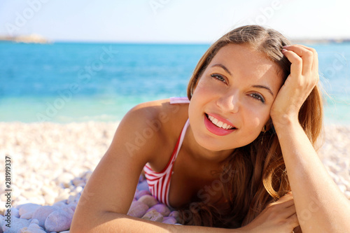 Summer Holidays concept. Young smiling woman enjoying relax lying on the beach looking at camera.