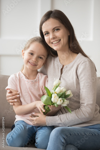Daughter holding tulips sitting with mom on couch at home