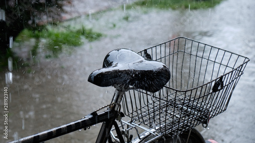 Heavy rain falling on a bicycle seat parked on sidewalk.  Focus on the seat, with rest heavily defocussed photo