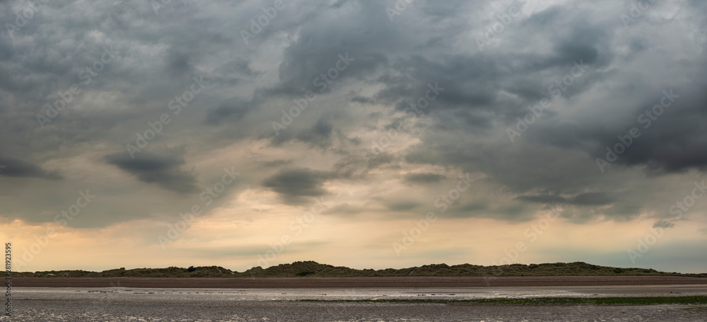 Beautiful panoramic landscape image of beach at low tide with dramatic storm clouds gathering overhead