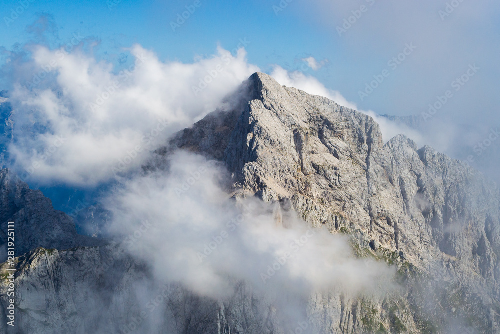 Jalovec ridge in the Julian Alps, Triglav National Park, Slovenia, with misty clouds and blue sky. Climbing, mountaineering, adventure in nature concepts. Jalovec ridge in the Julian Alps, Triglav National Park, Slovenia, with misty clouds and blue sky. Climbing, mountaineering, adventure in nature concepts.