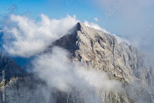 Jalovec ridge in the Julian Alps, Triglav National Park, Slovenia, with misty clouds and blue sky. Climbing, mountaineering, adventure in nature concepts.