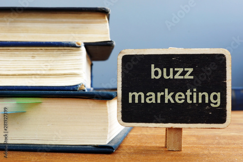 Text sign showing buzz marketing. The text is written on a small wooden blackboard. The book, pen, wooden background are on the photo.