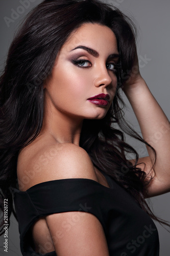 Beautiful bright makeup woman with long black curly hair style, burgundy lipstick with vamp look on grey background. Closeup