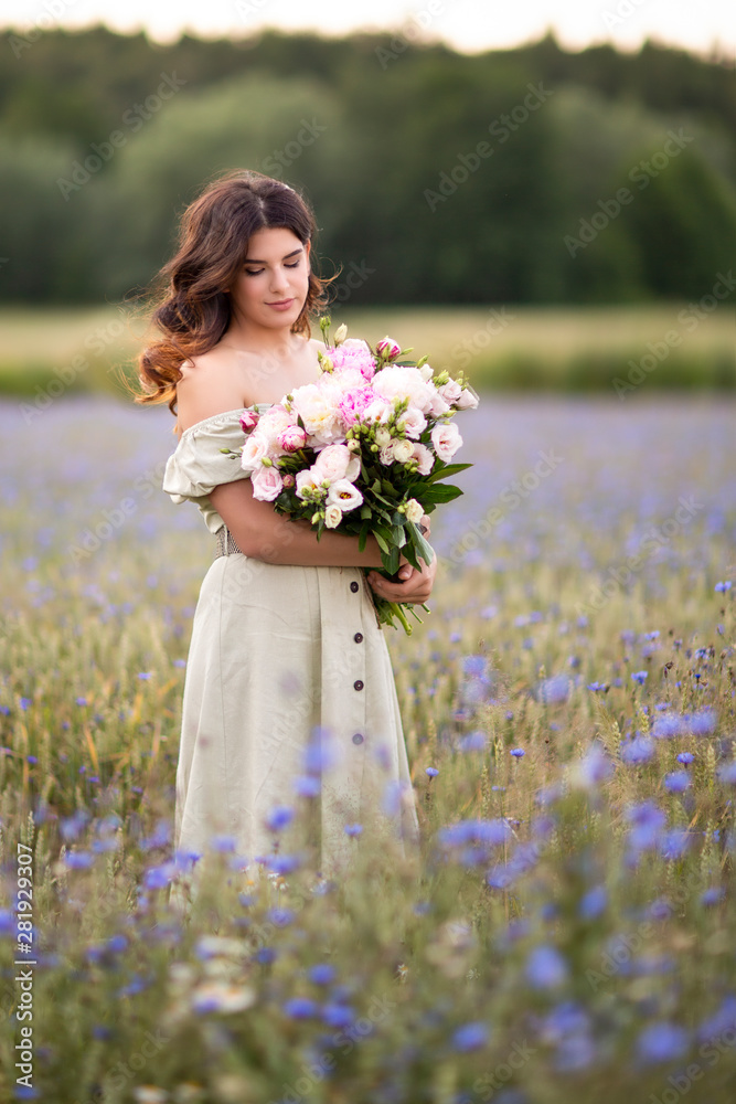 Fototapeta premium Young beautiful dark-haired girl with a bouquet of Peonies in a field of cornflowers. Summer.Cereals and field dawns. Life in the village.
