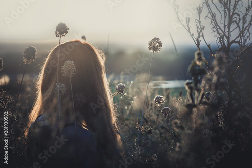 head backof red-haired girl sitting on the ground in a field among dried flowers and enjoys nature at sunset, young woman relaxing, concept of rest, healthcare, harmony, lifestyle