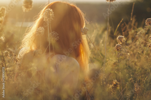 dreamy red-haired girl sits on the ground in a field among dried flowers and enjoys nature at sunset  young woman relaxing  concept of rest  healthcare  harmony  lifestyle