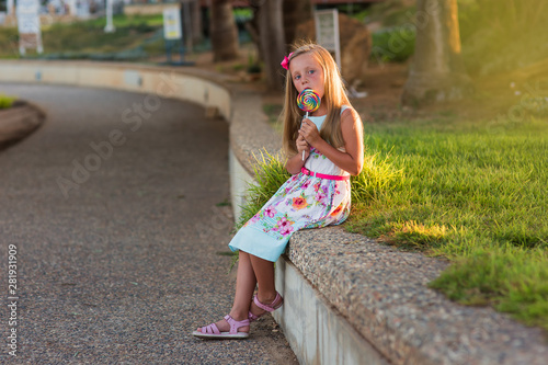 Portrait of a smiling girl with a lollipop at sunset in summer