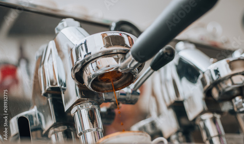 Coffee being brewed by the machine flowing through portafilter into the cup at cafe