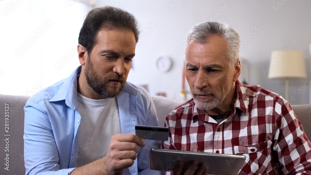 Son teaching father how to book tickets online, using tablet and credit card Son teaching father how to book tickets online, using tablet and credit card