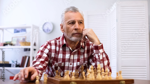 Aging pensive male playing chess alone, suffering loneliness in nursing home