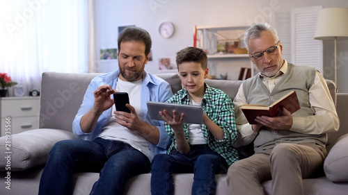 Middle-aged male and preteen boy scrolling gadgets, aging man reading paper book