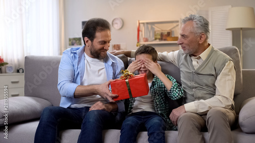 Caring father giving giftbox to little son with closed eyes, birthday surprise