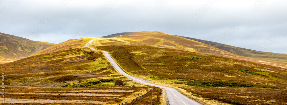 A scenic highway through bright yellow and brown highlands during autumn season in Cairngorms national park, Scotland
