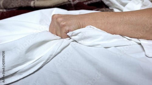 Terminally-ill woman clenching bedsheets feeling terrible pain, death convulsion