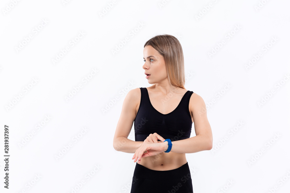 Young sporty blond woman in a black sportswear surprised havig checked pulse with smart watches after workout standing over white background.