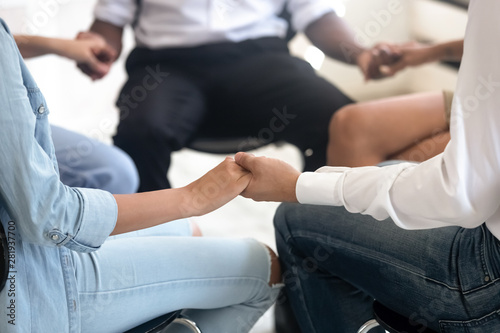 Closeup view people sitting on chairs in circle holding hands photo