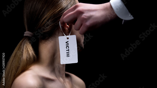 Male hand putting victim label on female ear, humiliation and bullying, close-up