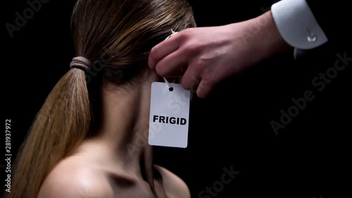 Man hand putting frigid label on female ear imposing sex insecurities on partner