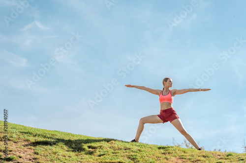 Harmonious lady practicing yoga warrior asana on hill