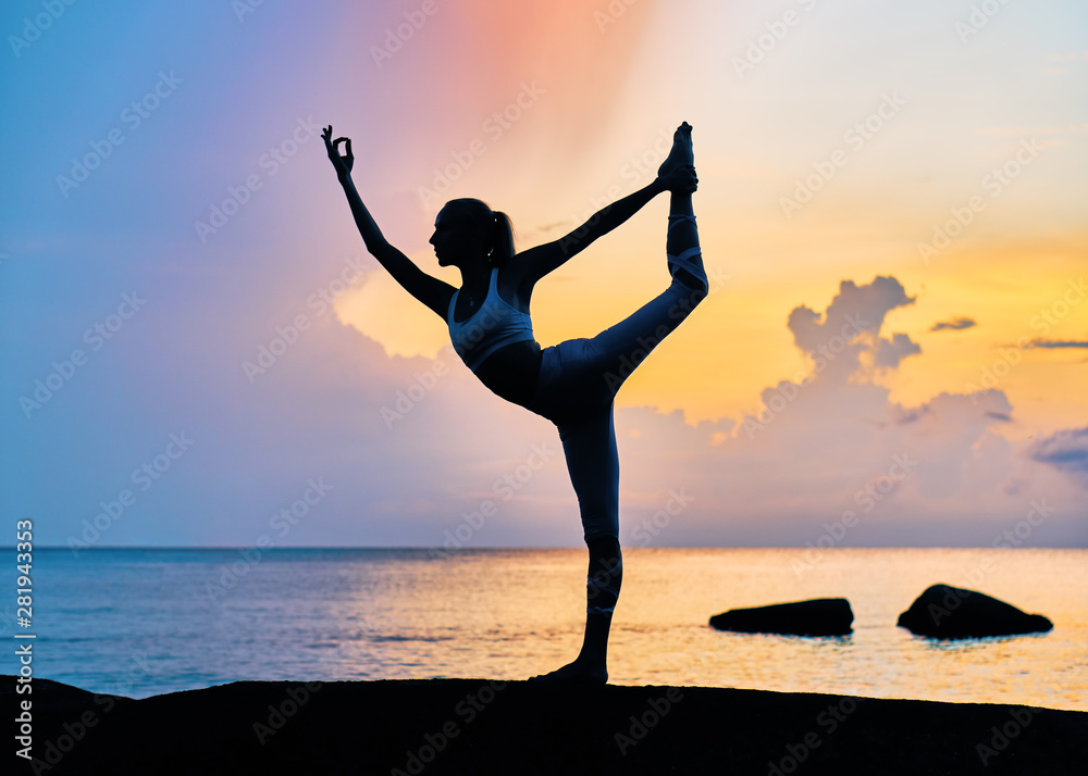 Slim woman doing yoga exercises by the sea at colourful sunrise