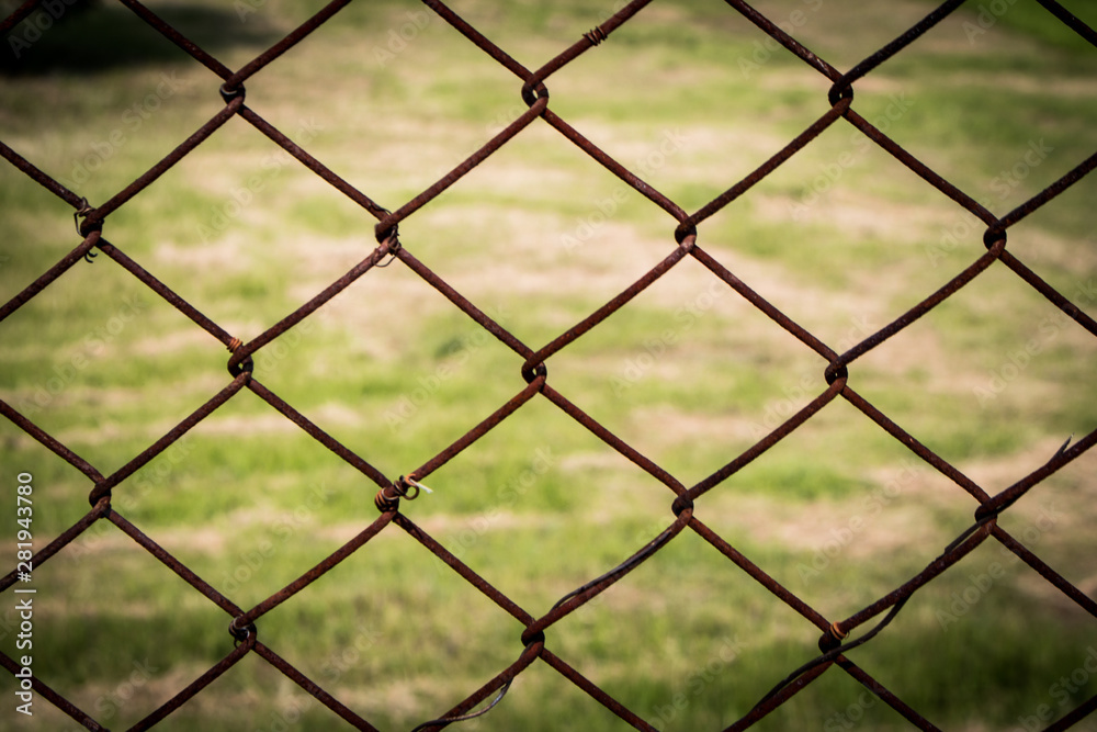 Naklejka premium The close up of brown wire fence (barricade) which is hardly rusted in blurred background (meadow).