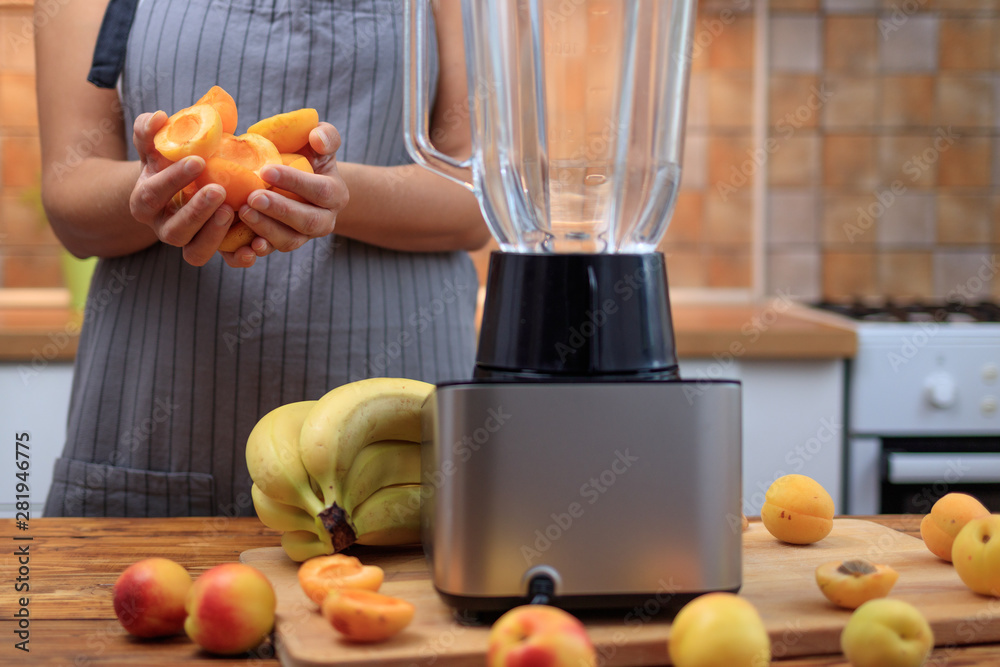 Woman preparing apricot smoothie or juice with fruits in the kitchen.