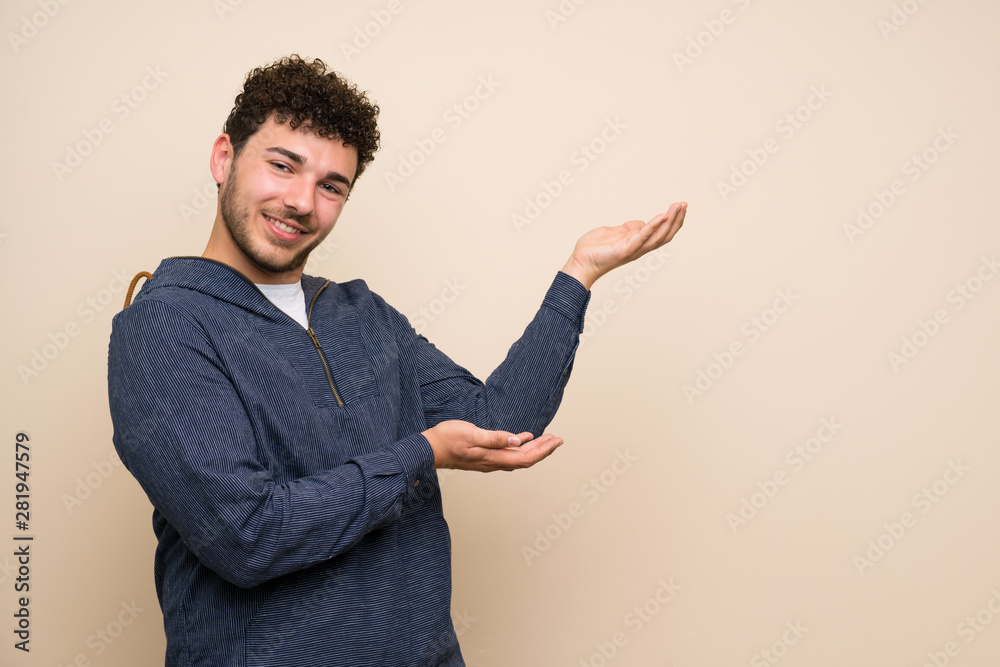 Man with curly hair over isolated wall extending hands to the side for inviting to come Man with curly hair over isolated wall extending hands to the side for inviting to come