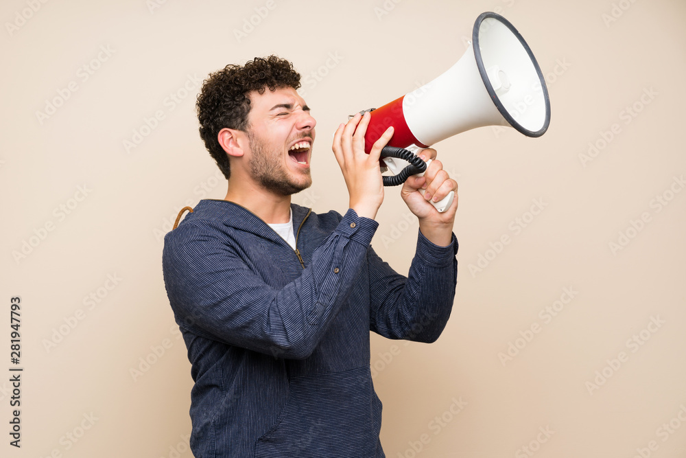 Man with curly hair over isolated wall shouting through a megaphone Man with curly hair over isolated wall shouting through a megaphone