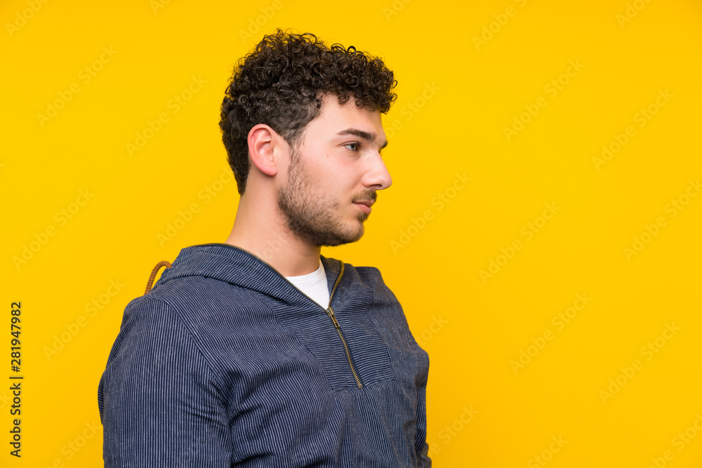 Fototapeta premium Young man over isolated yellow wall standing and looking side