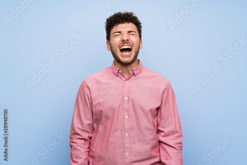 Man with curly hair over isolated blue wall shouting to the front with mouth wide open