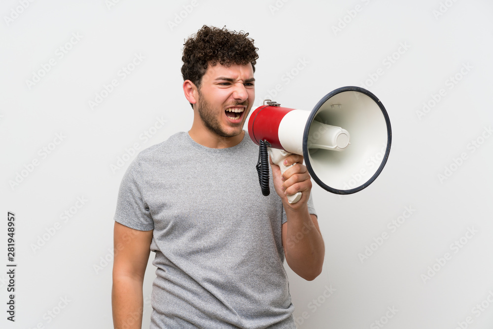 Man with curly hair over isolated wall shouting through a megaphone Man with curly hair over isolated wall shouting through a megaphone