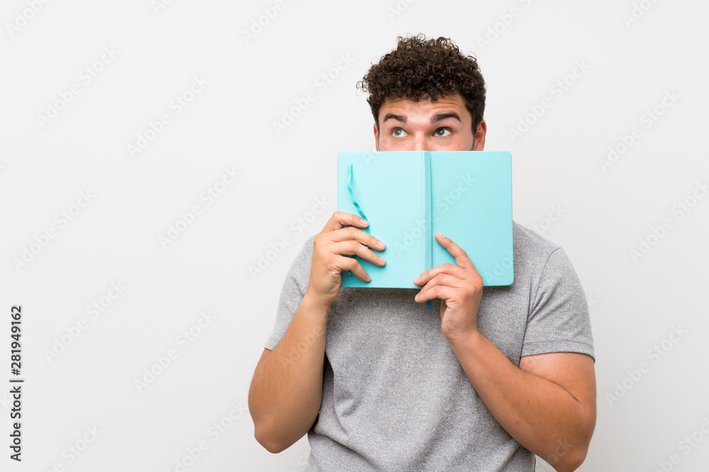 Man with curly hair over isolated wall holding and reading a book Man with curly hair over isolated wall holding and reading a book