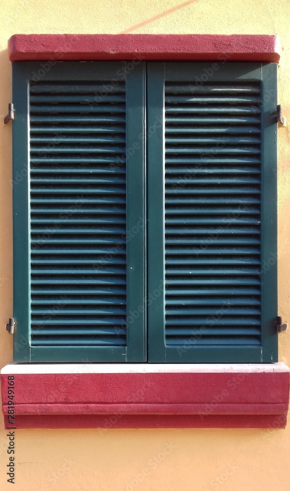 window with green shutters on orange wall
