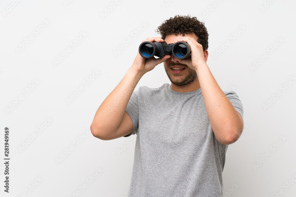 Man with curly hair over isolated wall with black binoculars Man with curly hair over isolated wall with black binoculars
