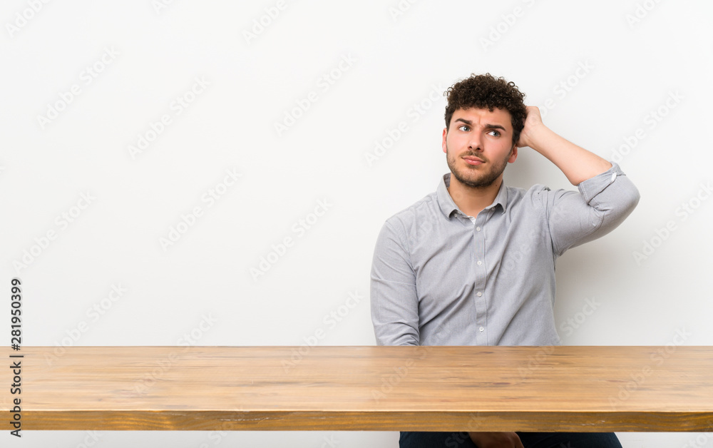 Young man with a table having doubts while scratching head Young man with a table having doubts while scratching head