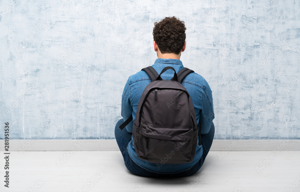 Young man sitting on the floor with backpack - obrazy, fototapety, plakaty 