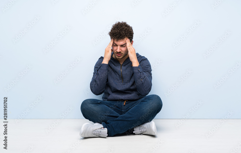 Young man sitting on the floor with headache Young man sitting on the floor with headache